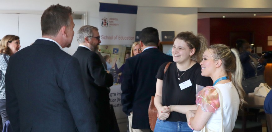 Two women speak stand in front of a table whilst talking to a male academic at Liverpool Hope's third sector networking event.